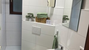 A bathroom with a toilet, sink, and shower area. There is a green towel on the floor and a small plant on the shelf. - Newly renovated apartment in the center of Hirschhorn / Neckar directly on the Neckarsteig (Hirschhorn)