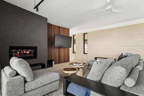 A modern living room with a fireplace, a flat-screen TV, and a ceiling fan.