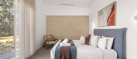 A modern bedroom with a large bed, a view of the outdoors, and a ceiling fan.