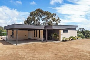 A modern building with a flat roof, a covered outdoor area, and a dirt ground.