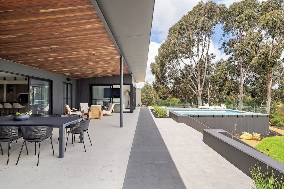 A modern outdoor patio with a dining area, a pool, and a view of trees.