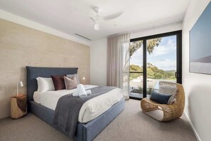 A modern bedroom with a large bed, a ceiling fan, a wicker chair, and a view of the outdoors.