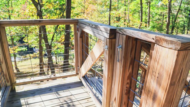 Eine Holzterrasse mit Metallgeländer, umgeben von Bäumen.