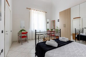 A bedroom with a bed, a desk, a chair, a mirror, and a window with curtains.