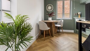 A compact kitchen with a round wooden table, two chairs, a potted plant, and a clock on the wall. - Pippin - BRAND NEW stylish studio apartment in the hub of Worcester City Centre (Worcestershire)