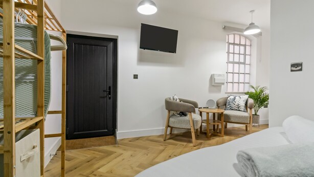 A bedroom with a bed, a desk, a chair, a TV, and a window. - Pippin - BRAND NEW stylish studio apartment in the hub of Worcester City Centre (Worcestershire)
