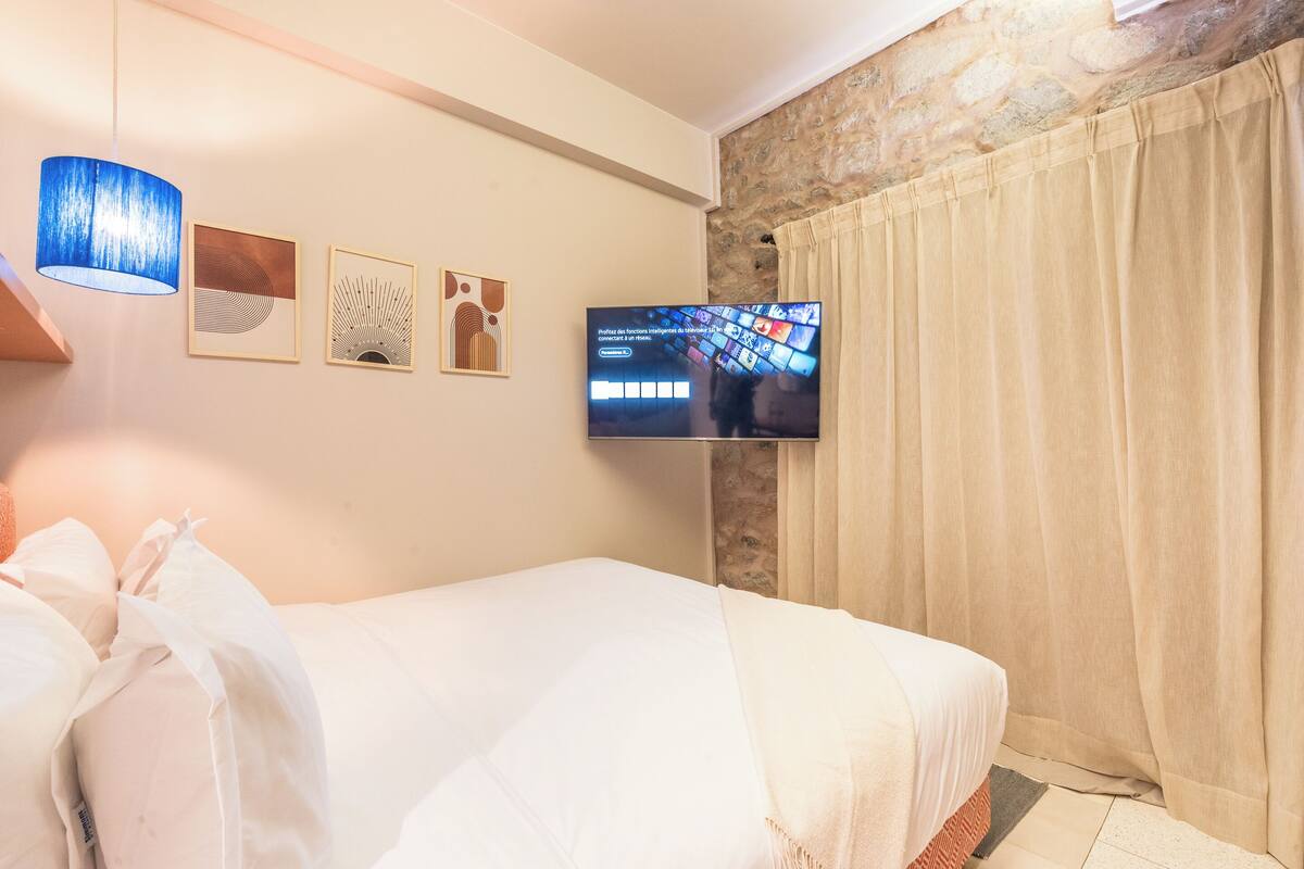 A hotel room with a bed, a television mounted on the wall, and a stone wall.
