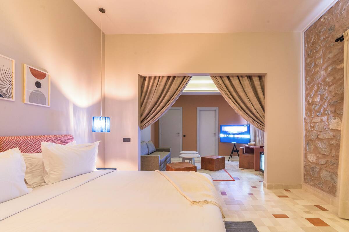 A hotel room with a large bed, a TV, a desk, and a stone wall.