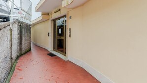 Un pasillo estrecho con suelo de baldosas rojas, pared color beige y una puerta de cristal que da a una habitación.