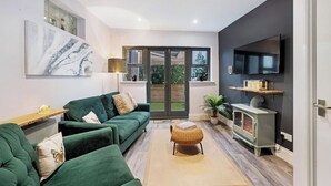 Uma sala de estar moderna com um sofá verde, uma televisão de tela plana, uma lareira a lenha e uma janela grande.
