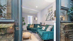 Uma sala de estar moderna com um sofá verde, um banquinho de vime e uma parede de pedra.