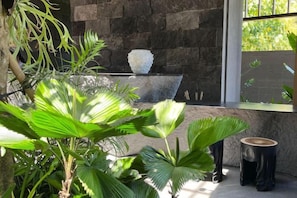 Un mur de pierre agrémenté d’un vase décoratif, une fenêtre donnant sur un paysage verdoyant et une plante en pot.