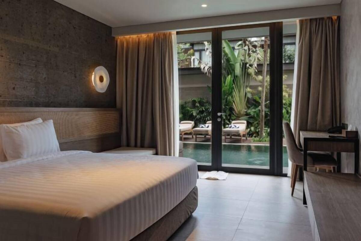 Een moderne hotelkamer met een groot bed, een bureau en uitzicht op een buitenzwembad.