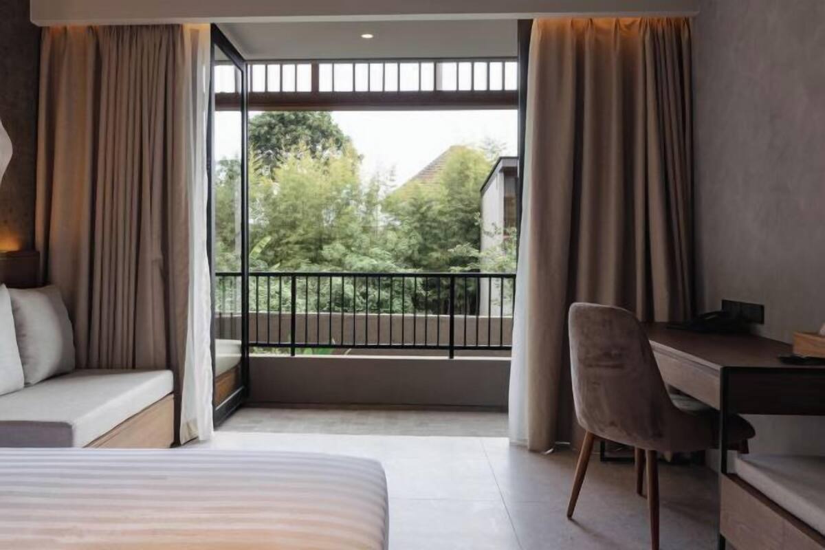Een slaapkamer met een bed, een bureau en uitzicht op een balkon met een hekwerk.