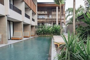A pool area with lounge chairs and a building with balconies. - The Akasha Canggu Hotel (Bali)