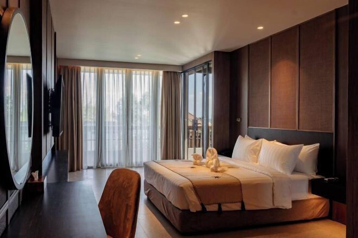 Hotelkamer met een groot bed, een bureau en een stoel. Er is een groot raam met gordijnen.
