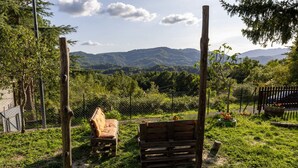 Un espacio de estar al aire libre rústico con bancos de madera y una cerca, rodeado de exuberante vegetación y montañas al fondo.