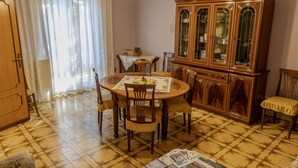 Un comedor con una mesa redonda, sillas, un aparador de madera con puertas de cristal y una araña.