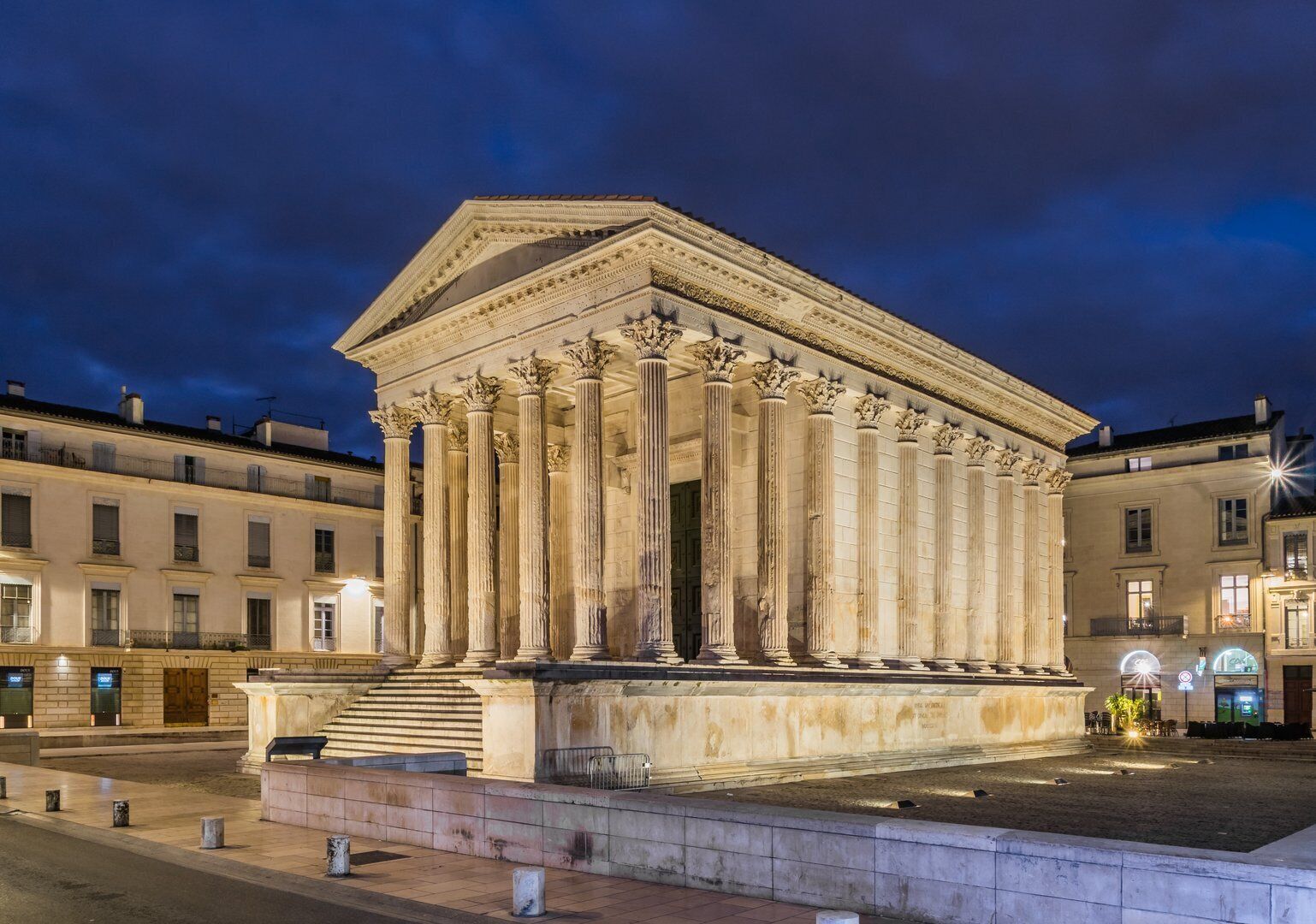 Un bâtiment de style classique, doté de colonnes, d’une entrée centrale et d’une zone pavée qui l’entoure.