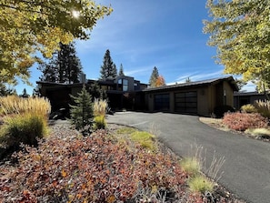 A modern house with a driveway, surrounded by autumn foliage and tall trees.