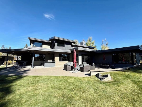 A modern two-story house with a covered patio area, outdoor furniture, and a well-maintained lawn.