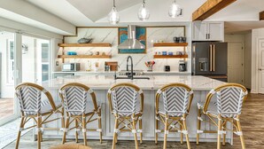 Una cocina moderna con una isla central, cuatro sillas de mimbre, lámparas colgantes y electrodomésticos integrados.