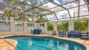 Una piscina con cerramiento de vidrio, rodeada de mobiliario exterior y palmeras.