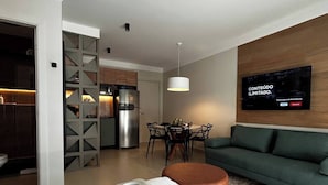 Una sala de estar moderna con un sofá verde, un comedor con mesa y sillas, y una cocina con refrigerador y cafetera.