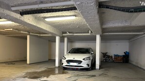 Une voiture blanche était garée dans un parking souterrain aux murs de béton, faiblement éclairé, et on pouvait voir des taches d’eau sur le sol.