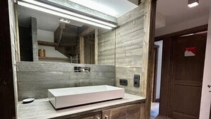 Une salle de bain moderne avec un grand miroir, un lavabo blanc, des meubles en bois et un sol carrelé.