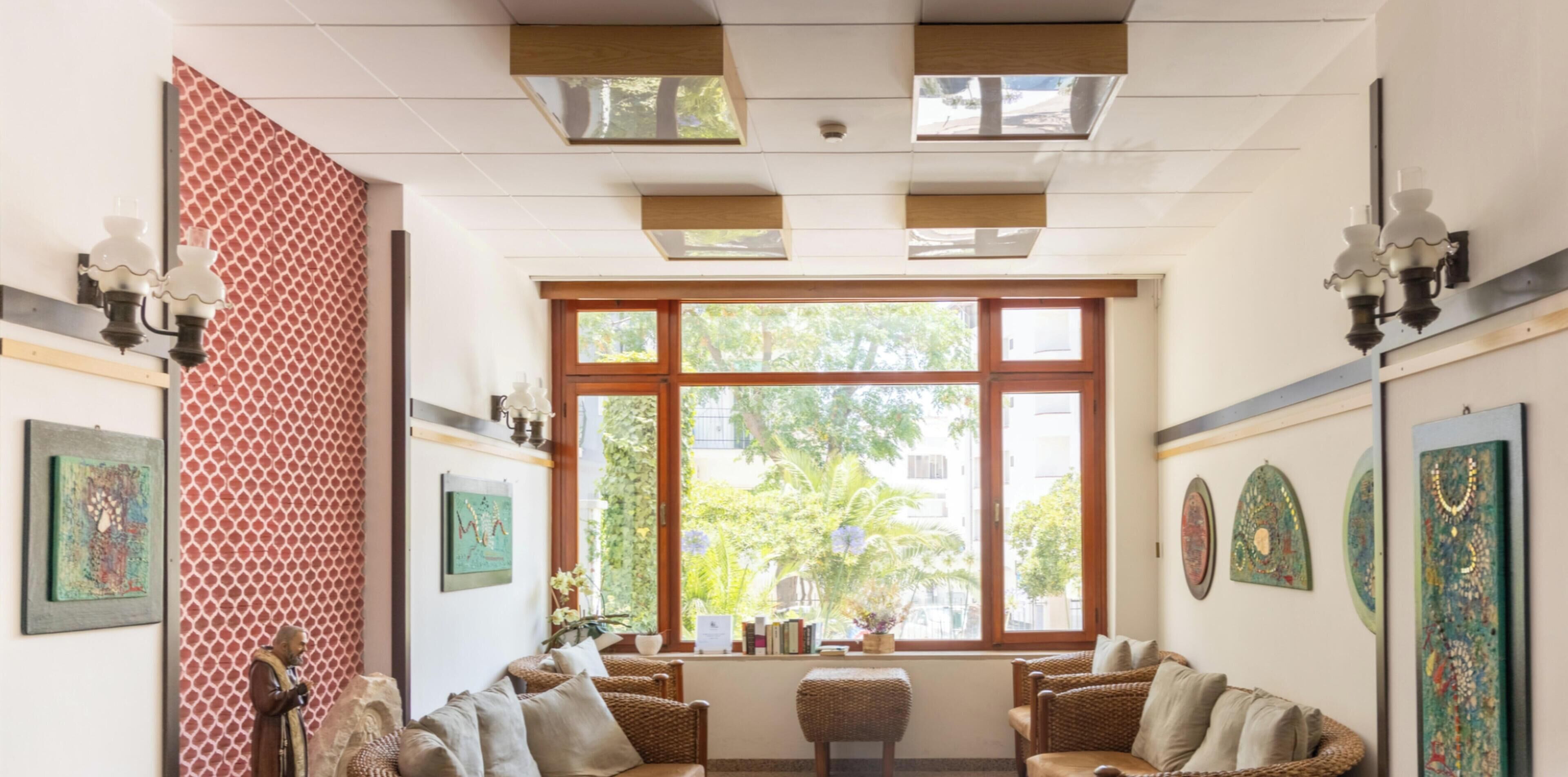 Ein Zimmer mit großem Fenster, Korbmöbeln, an der Wand befestigter Kunst und Deckenleuchten.