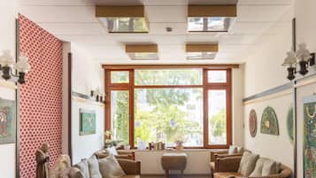Ein Zimmer mit großem Fenster, Korbmöbeln, an der Wand befestigter Kunst und Deckenleuchten.