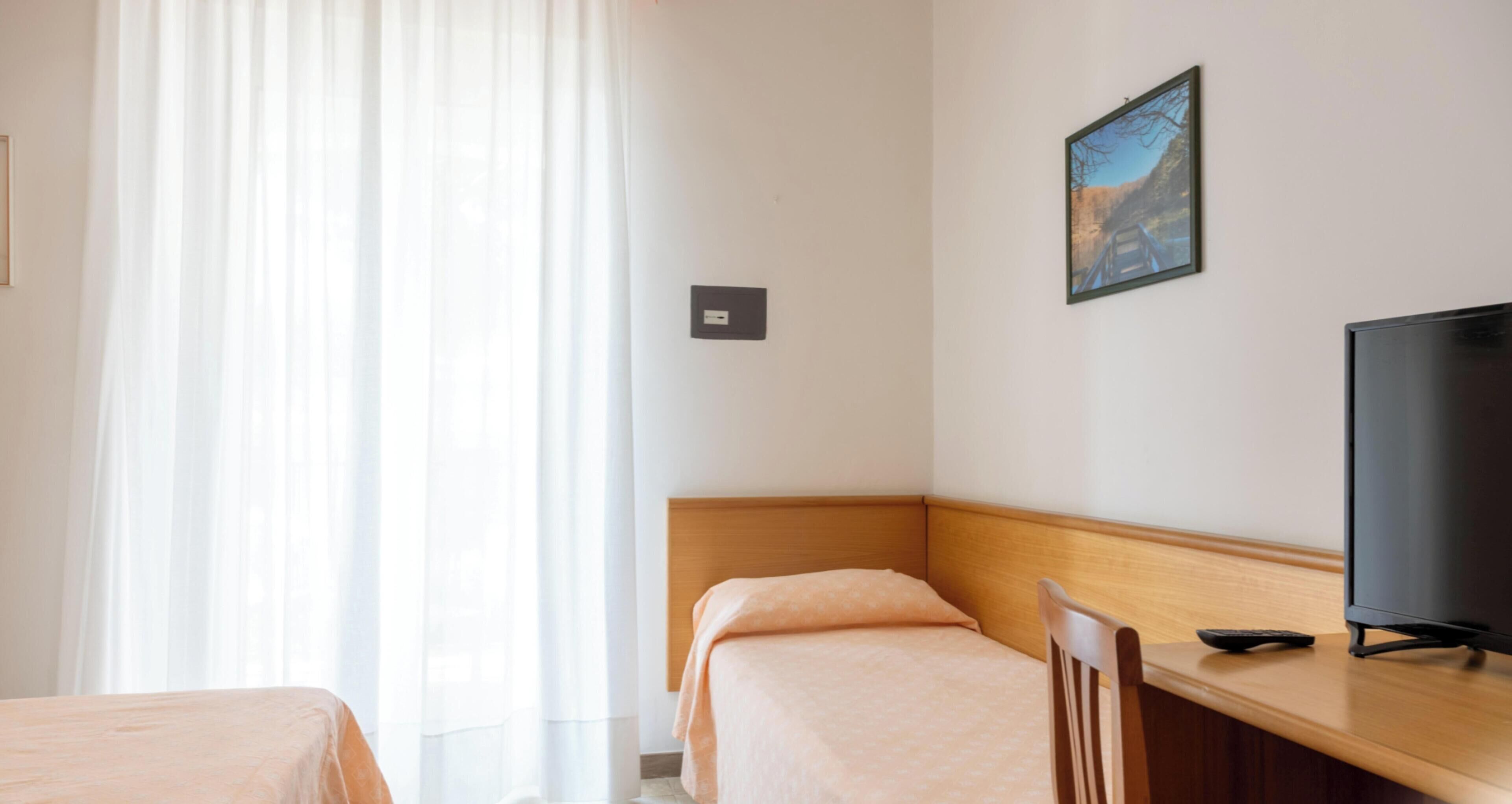 Une chambre d’hôtel avec deux lits simples, une tête de lit en bois, un téléviseur posé sur un bureau en bois et un tableau encadré accroché au mur.