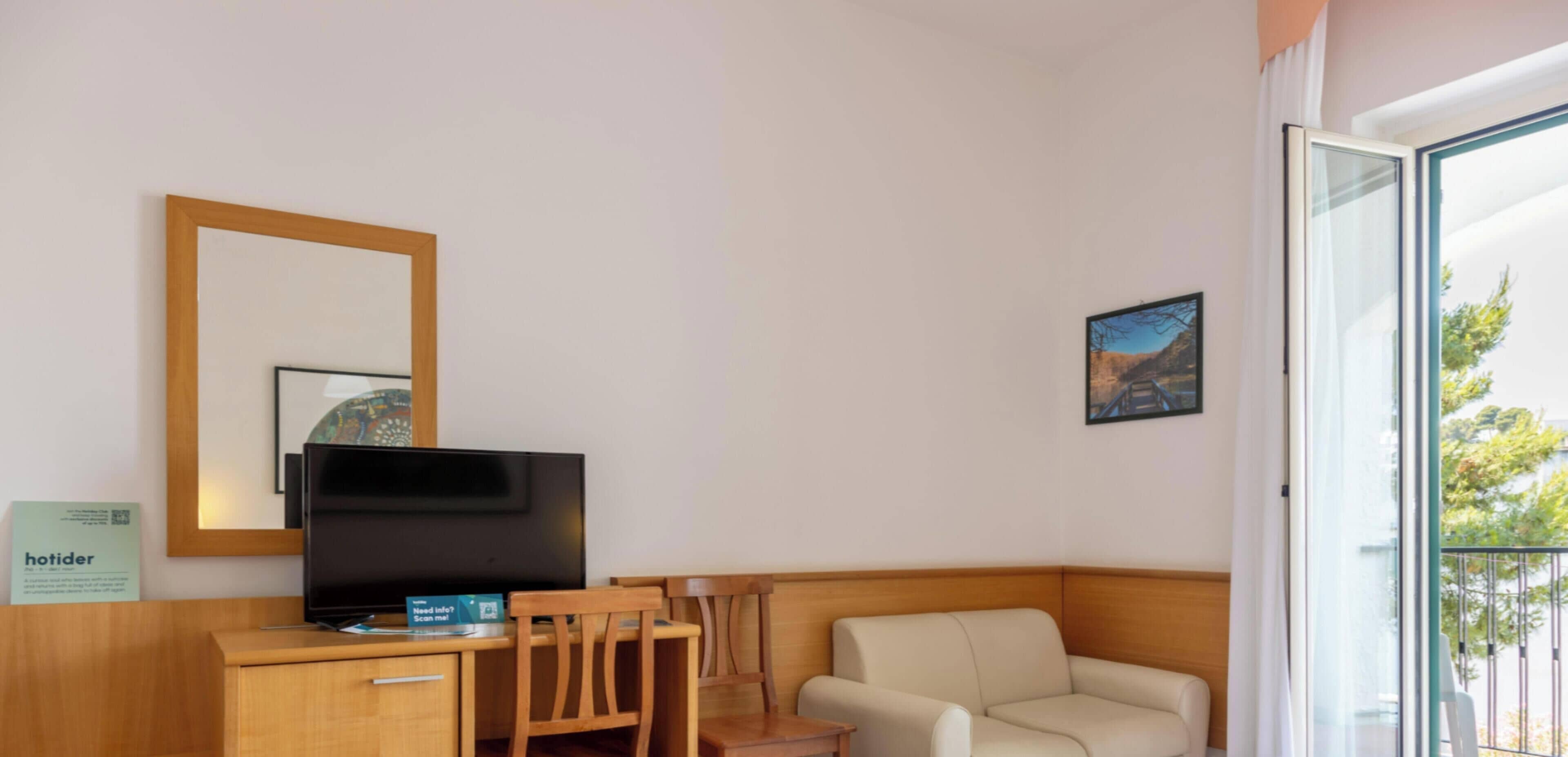 Habitación de hotel con televisión, muebles de madera, sofá, una mesita y balcón con vistas.