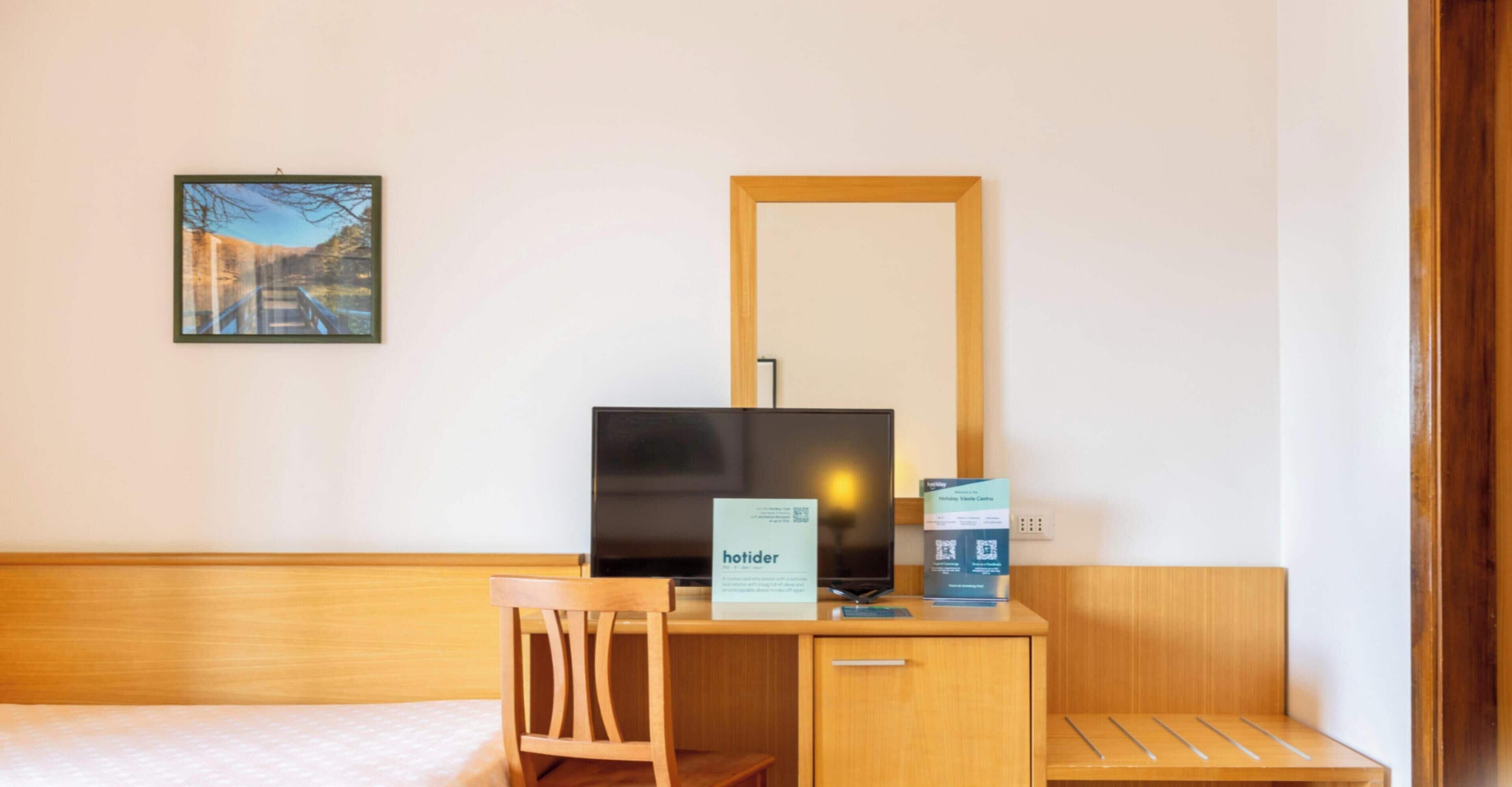 A hotel room with a bed, a desk with a chair, a television, and a mirror.