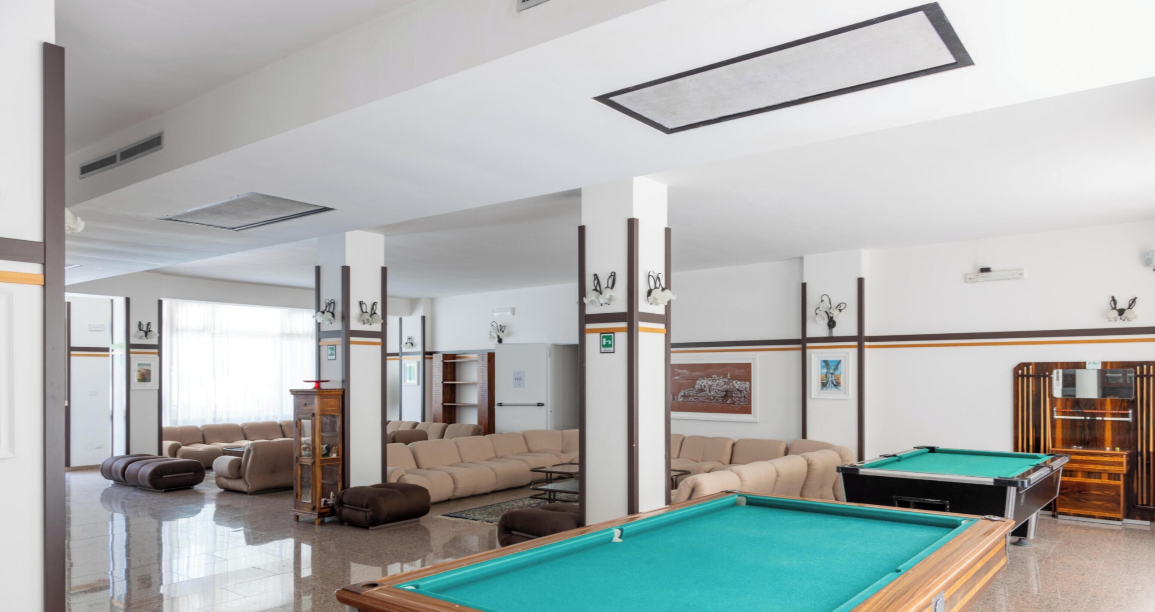 Une table de billard, plusieurs canapés et un espace dédié au billard dans une pièce bien éclairée, dotée d’un plafond haut et d’un décor moderne.