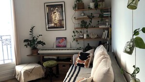 A cozy living room with a sofa, a piano, and a bookshelf filled with books and plants. - Bright apartment with balcony (Clichy)