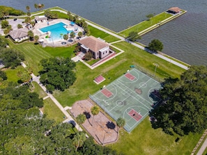 An aerial view of a residential property with a swimming pool, tennis courts, and a house.