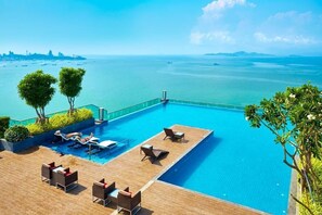 Une piscine à débordement située sur le toit, avec des chaises longues et une vue sur l’océan.