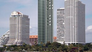 Three high-rise hotels with multiple balconies, a beach in the foreground, and palm trees.
