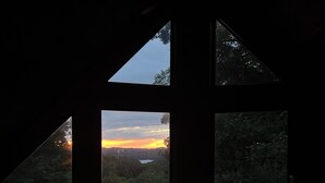Blick durch ein Fenster auf einen Sonnenuntergang über einem bewaldeten Gebiet.