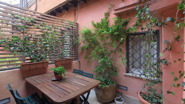 A wooden table with chairs, potted plants, and a window with a metal grille. - "Elegant 2 Level Duplex 2 Baths & Bikes -Trastevere" (Roma)