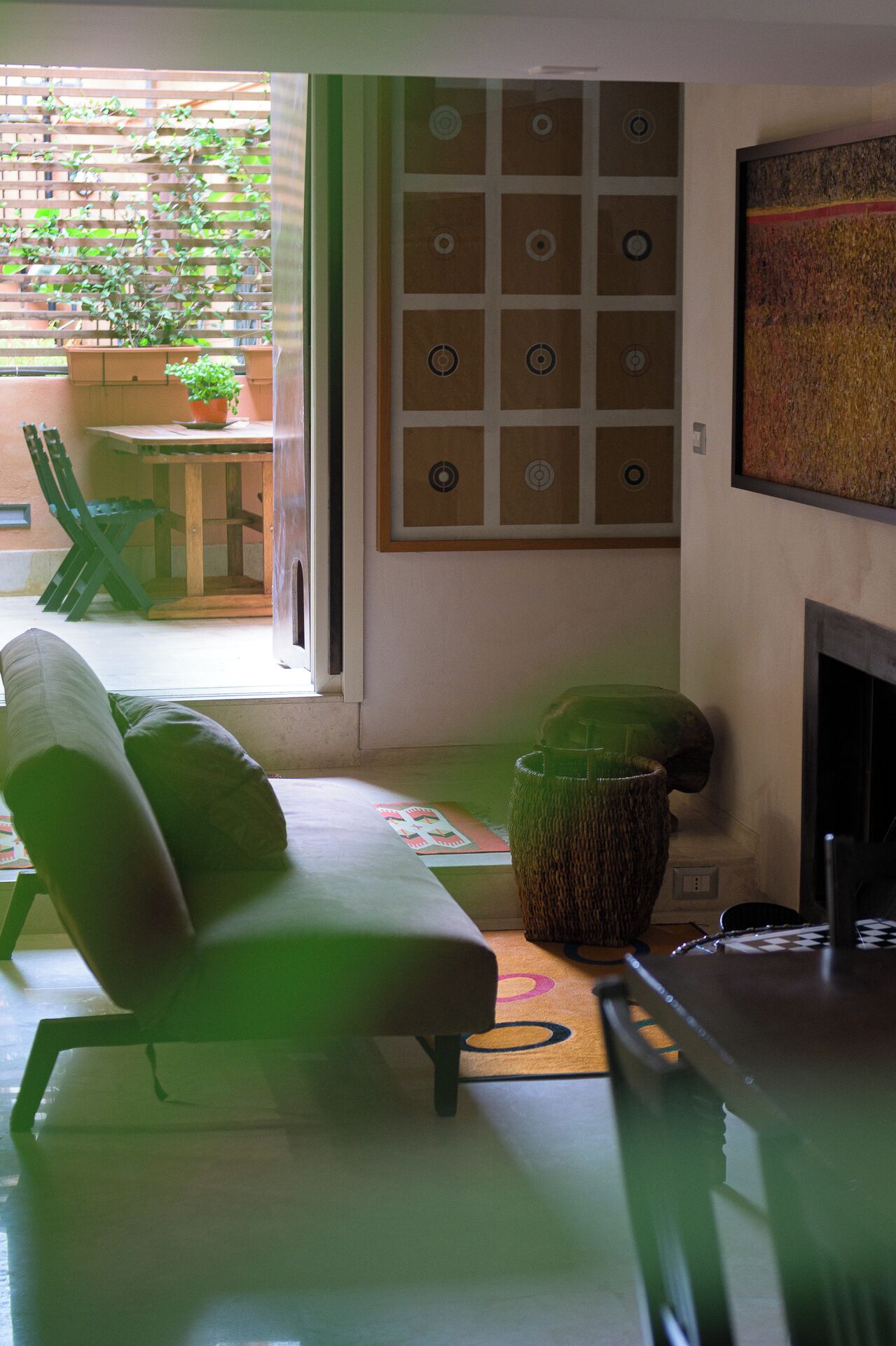 A modern living room with a sofa, a coffee table, and a fireplace. There is a window with a view of greenery outside.