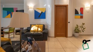 Ein modernes Wohnzimmer mit einer Couch, einer Lampe und einem Couchtisch. An den Wänden befinden sich abstrakte Gemälde und ein Blumentopf.