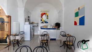Ein Essbereich eines Hotels mit Tischen und Stühlen, eine Küche im Hintergrund und ein großes abstraktes Gemälde an der Wand.