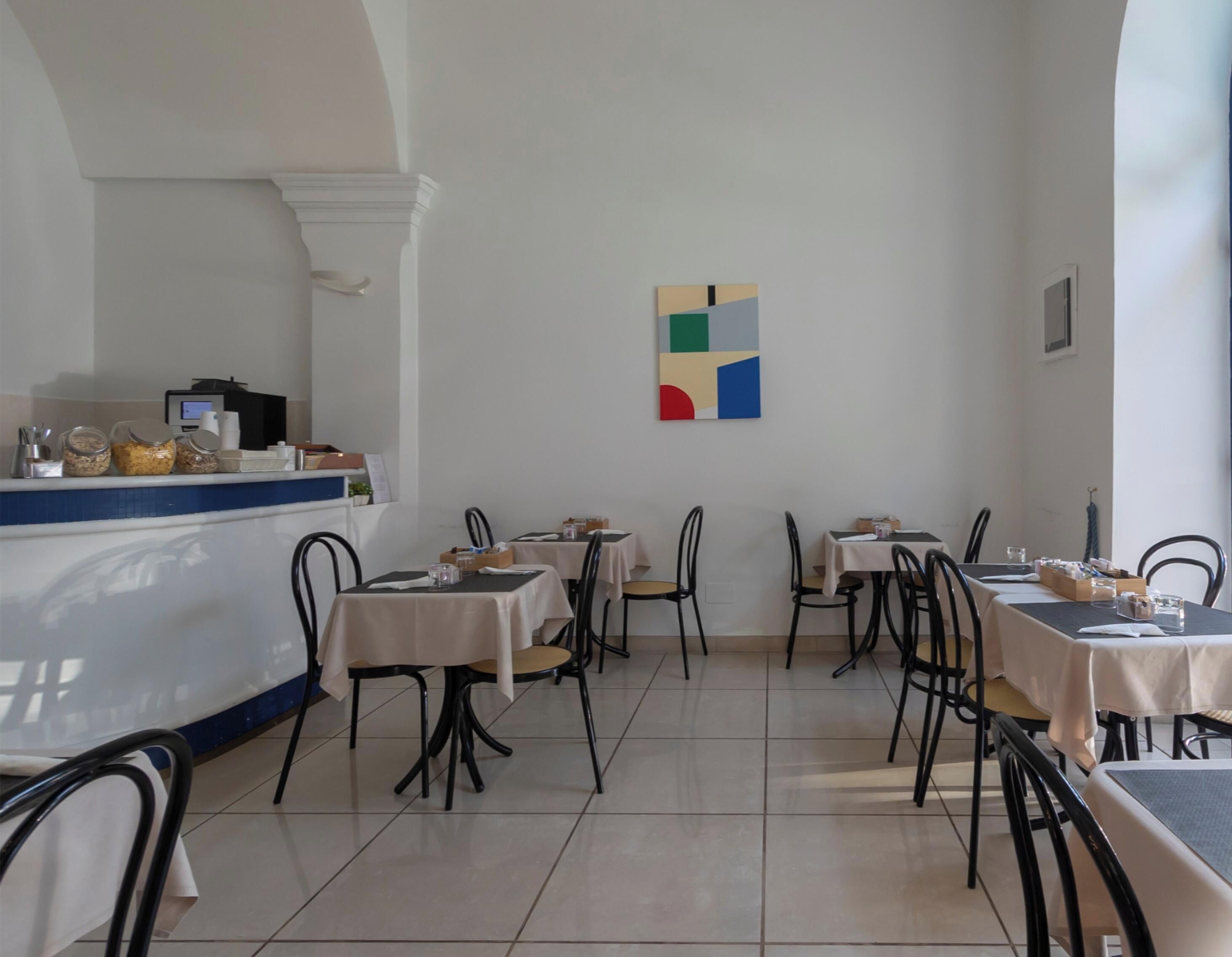 Ein Restaurant mit mehreren Tischen und Stühlen, einer Theke voller Speisen und einem Kunstwerk an der Wand.