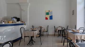 Ein Restaurant mit mehreren Tischen und Stühlen, einer Theke voller Speisen und einem Kunstwerk an der Wand.