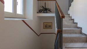 Eine Treppe mit Marmorstufen, einem hölzernen Geländer und einem Blumentopf auf der Podestfläche.