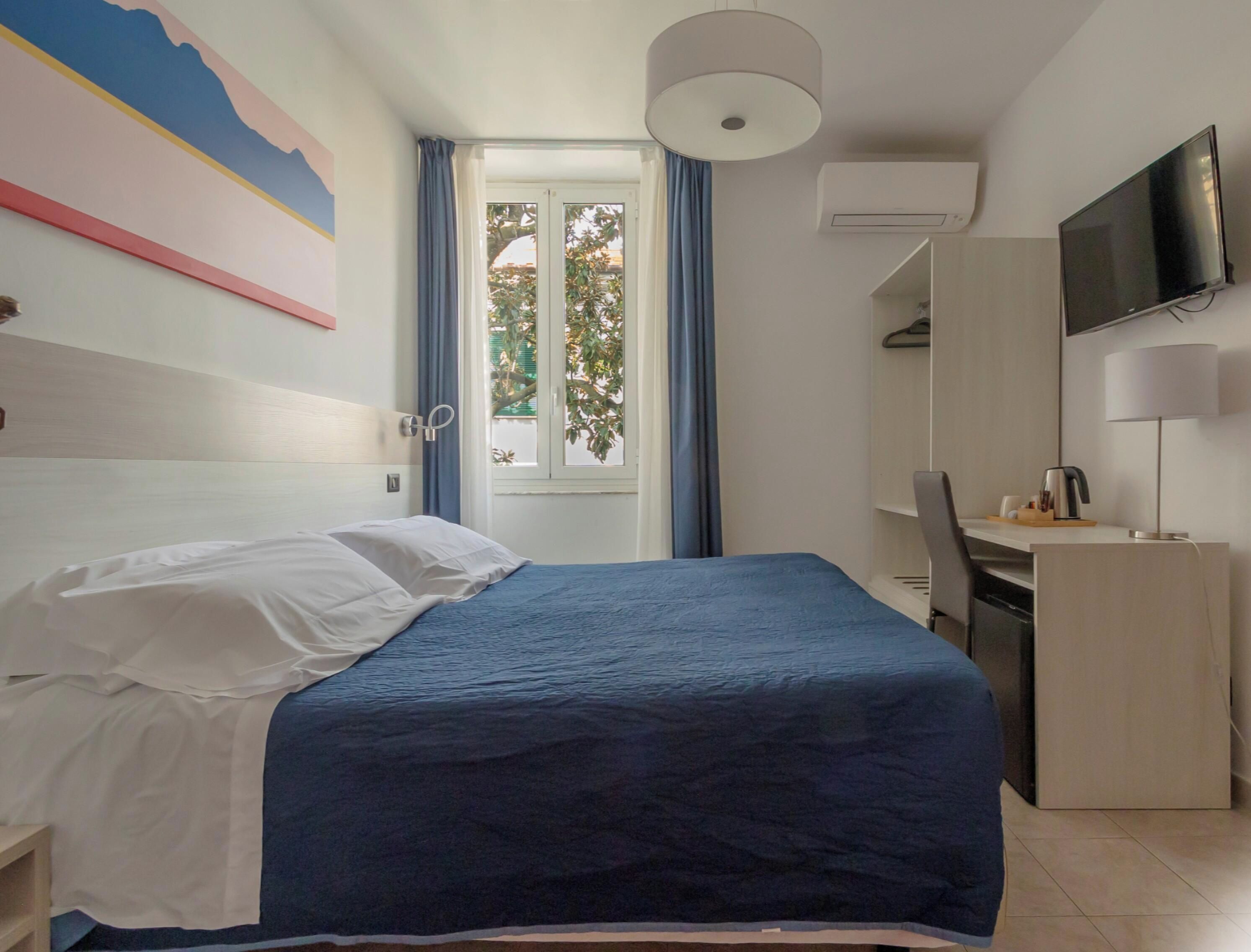 Ein Hotelzimmer mit Bett, Schreibtisch, Fernseher und einem Fenster mit Vorhängen.