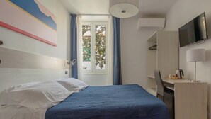 Ein Hotelzimmer mit Bett, Schreibtisch, Fernseher und einem Fenster mit Vorhängen.
